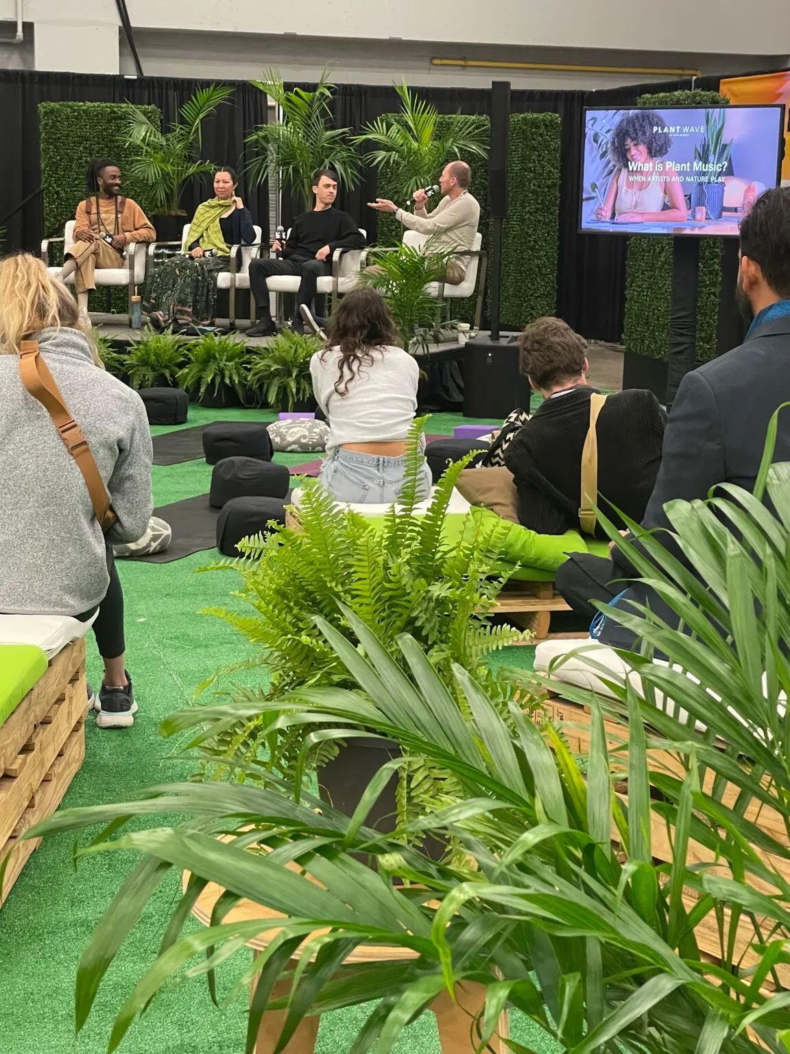 A panel discussion with plants surrounding the stage and a screen reading What Is Plant Music?